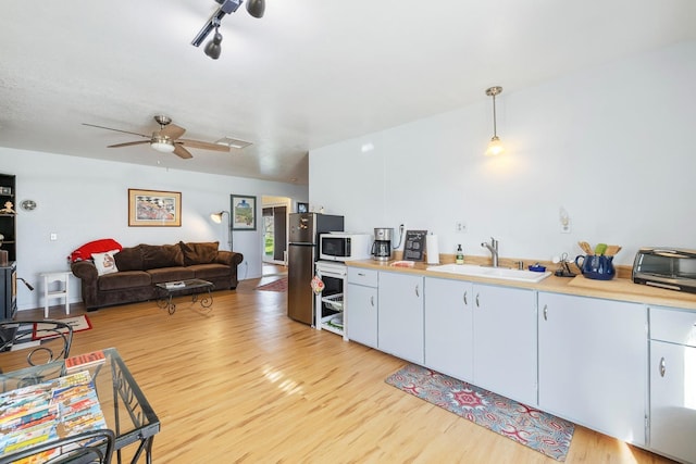 kitchen with light wood finished floors, white microwave, hanging light fixtures, light countertops, and a sink