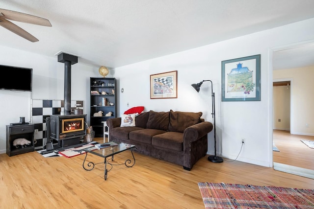 living area featuring a wood stove, baseboards, a ceiling fan, and wood finished floors