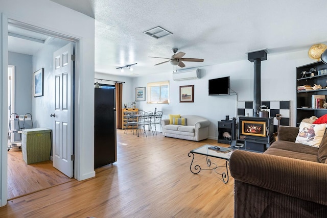 living area featuring a textured ceiling, ceiling fan, light wood-style flooring, an AC wall unit, and a wood stove