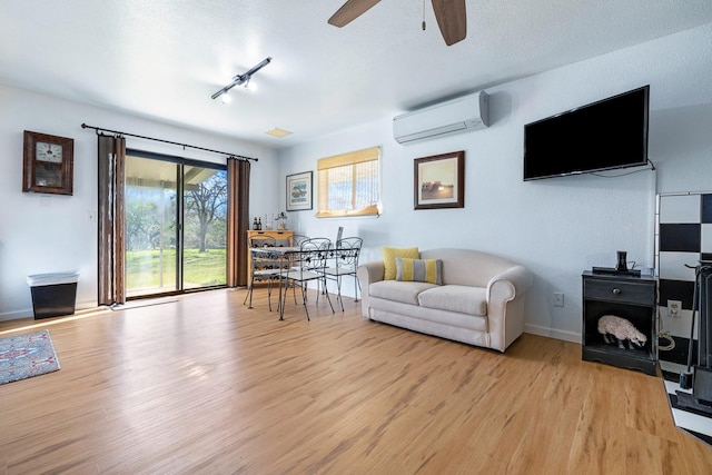 living area with light wood finished floors, ceiling fan, rail lighting, and a wall mounted air conditioner