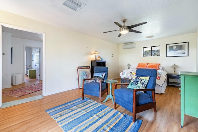 bedroom with visible vents, a wall mounted air conditioner, light wood-style flooring, and baseboards