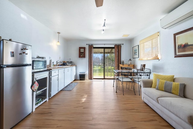 kitchen featuring light wood-style flooring, a wall mounted air conditioner, stainless steel appliances, white cabinetry, and a sink