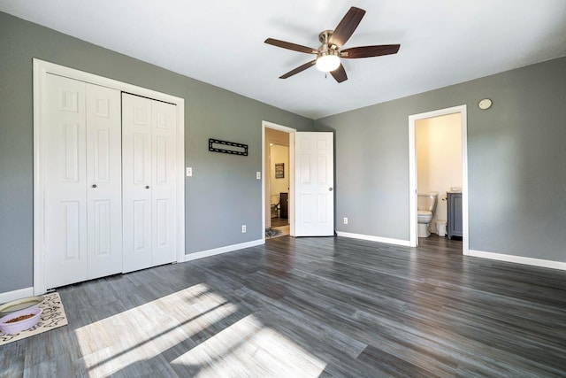 unfurnished bedroom with baseboards, ensuite bath, ceiling fan, dark wood-style flooring, and a closet