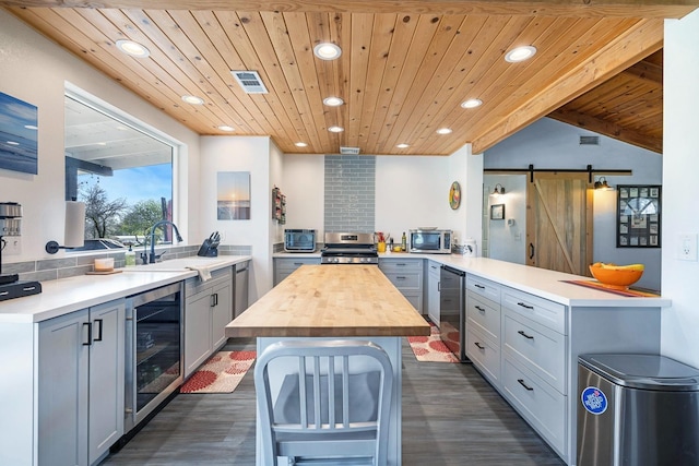 kitchen with a barn door, beverage cooler, wood counters, visible vents, and appliances with stainless steel finishes