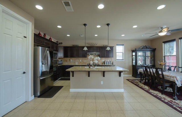 kitchen featuring light stone counters, visible vents, a kitchen breakfast bar, appliances with stainless steel finishes, and a center island