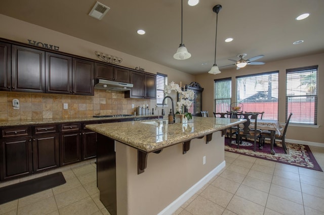 kitchen with visible vents, a kitchen breakfast bar, backsplash, under cabinet range hood, and a sink