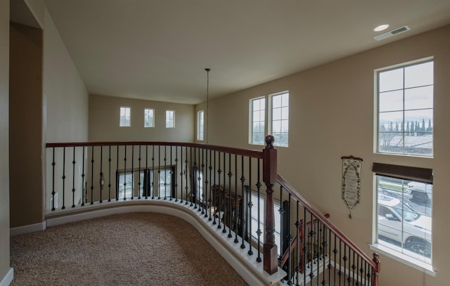 hall featuring carpet flooring, a towering ceiling, an upstairs landing, visible vents, and baseboards