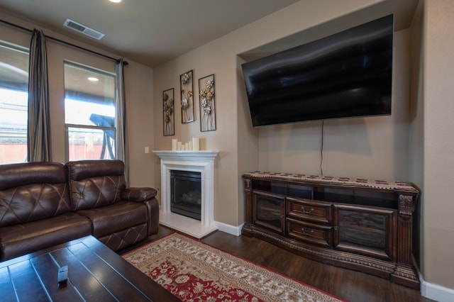 living area with a fireplace with raised hearth, wood finished floors, visible vents, and baseboards