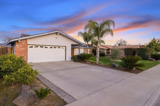 ranch-style house featuring an attached garage, brick siding, concrete driveway, a lawn, and stucco siding