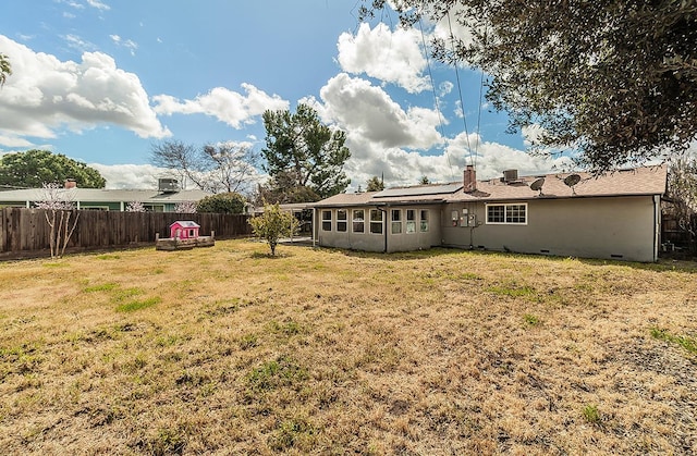 back of property featuring roof mounted solar panels, a fenced backyard, and a yard