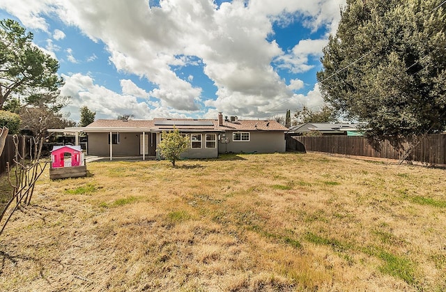 back of house featuring stucco siding, a fenced backyard, solar panels, and a yard