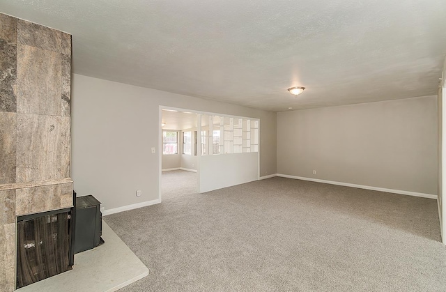 unfurnished living room with carpet, a fireplace, a textured ceiling, and baseboards