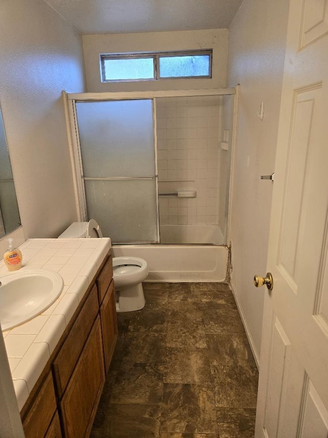 bathroom with toilet, shower / bath combination with glass door, stone finish floor, and vanity