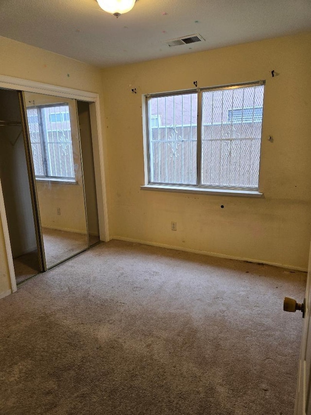 unfurnished bedroom featuring visible vents, a closet, carpet flooring, and multiple windows
