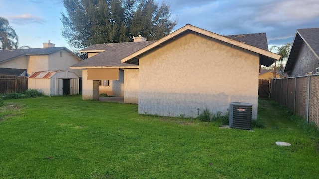 rear view of house featuring central AC unit, a lawn, a fenced backyard, a shed, and stucco siding