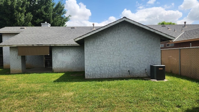 rear view of house with a yard, a shingled roof, stucco siding, and central AC unit
