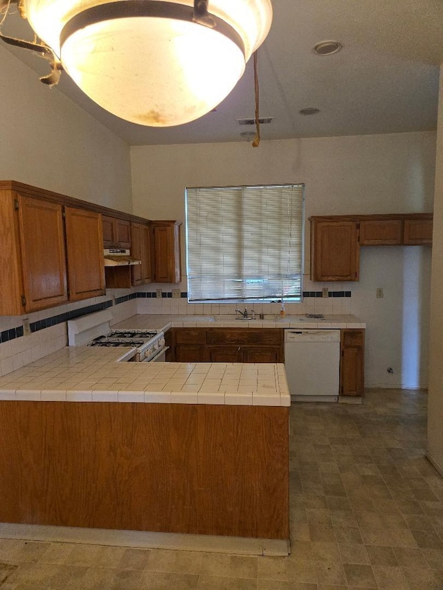 kitchen featuring tasteful backsplash, brown cabinetry, white appliances, and under cabinet range hood