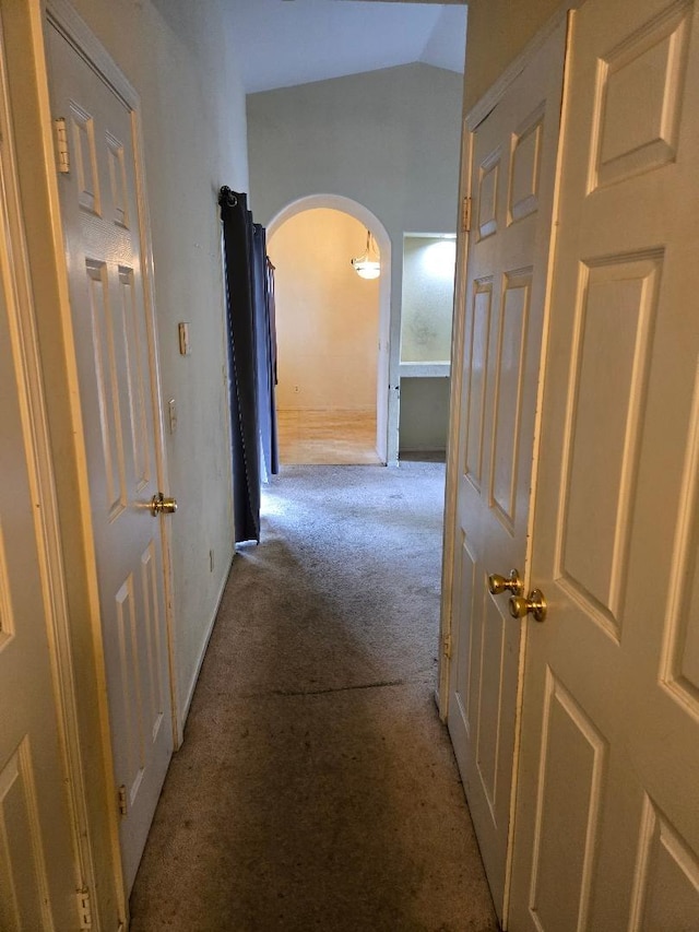 hallway featuring lofted ceiling, baseboards, arched walkways, and carpet floors