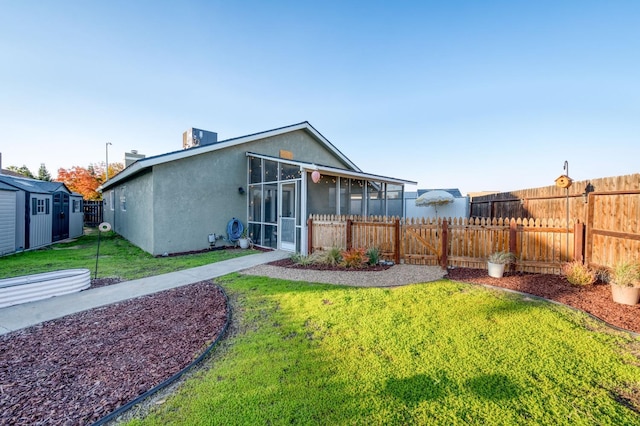 rear view of house featuring an outbuilding, stucco siding, a lawn, a sunroom, and fence