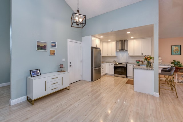 kitchen featuring light wood-style flooring, decorative backsplash, appliances with stainless steel finishes, white cabinets, and wall chimney range hood