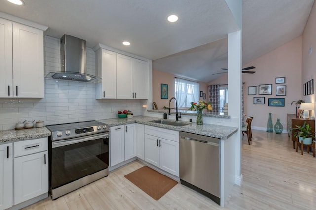 kitchen featuring appliances with stainless steel finishes, a peninsula, light wood-type flooring, wall chimney range hood, and a sink