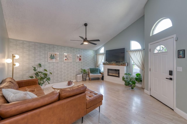 living room with wallpapered walls, baseboards, a ceiling fan, a glass covered fireplace, and light wood-style flooring