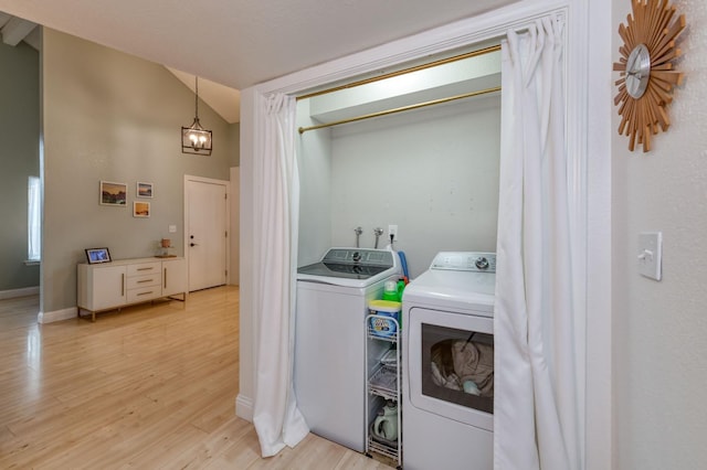 clothes washing area with light wood-style floors, washing machine and dryer, baseboards, and an inviting chandelier