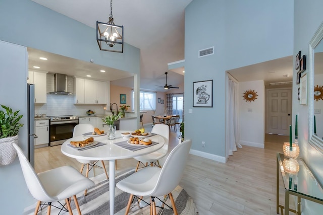 dining space with light wood-style floors, baseboards, a high ceiling, and visible vents