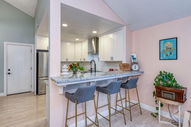 kitchen with white cabinetry, light wood-style floors, freestanding refrigerator, light stone countertops, and wall chimney exhaust hood