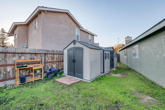 back of house featuring a storage shed, a lawn, fence, an outdoor structure, and stucco siding