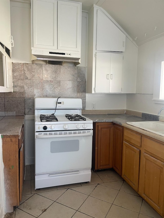 kitchen with under cabinet range hood, a sink, white cabinets, vaulted ceiling, and white range with gas cooktop