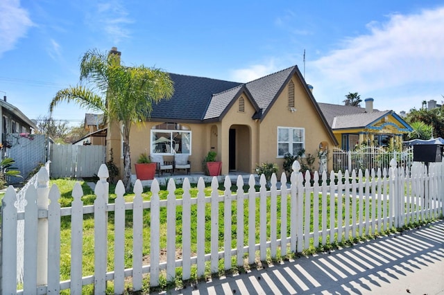 english style home featuring a fenced front yard, a chimney, and stucco siding