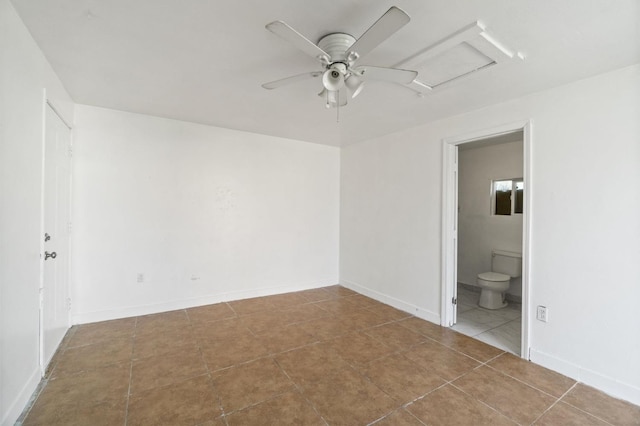 tiled empty room with attic access, baseboards, and ceiling fan