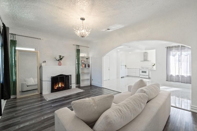 living area with arched walkways, a textured ceiling, a fireplace with flush hearth, and visible vents