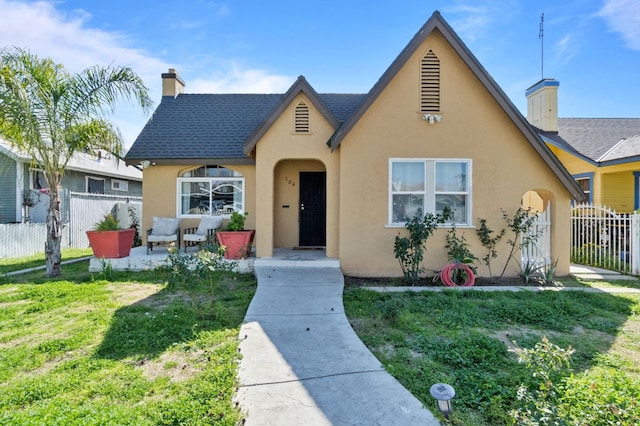 tudor home with fence, a chimney, a front lawn, and stucco siding