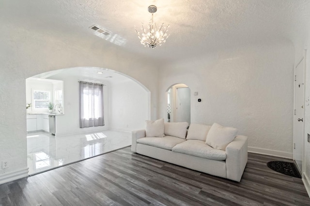 living room featuring a textured ceiling, visible vents, arched walkways, and wood finished floors