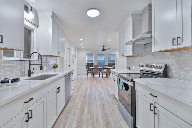 kitchen featuring stainless steel appliances, light wood-style floors, white cabinetry, a sink, and wall chimney range hood