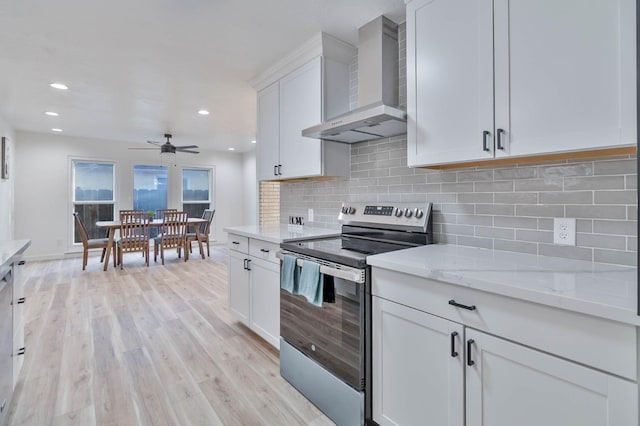 kitchen with light wood finished floors, decorative backsplash, wall chimney exhaust hood, stainless steel electric range, and white cabinetry