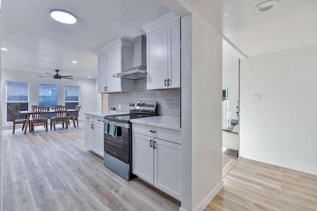 kitchen featuring wall chimney range hood, stainless steel electric range oven, light countertops, and light wood-style floors