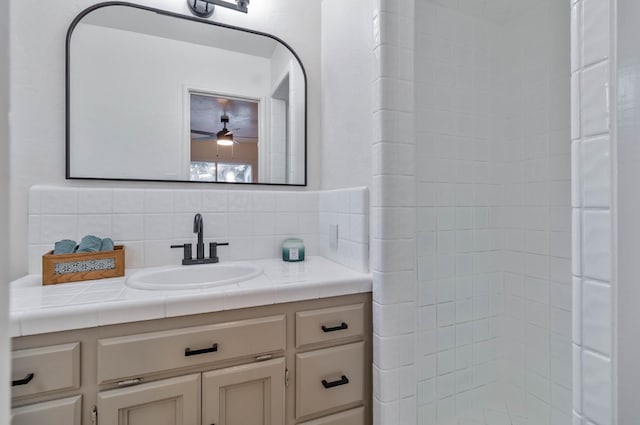 full bathroom featuring ceiling fan, a tile shower, backsplash, and vanity