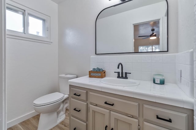 bathroom with toilet, ceiling fan, wood finished floors, vanity, and backsplash