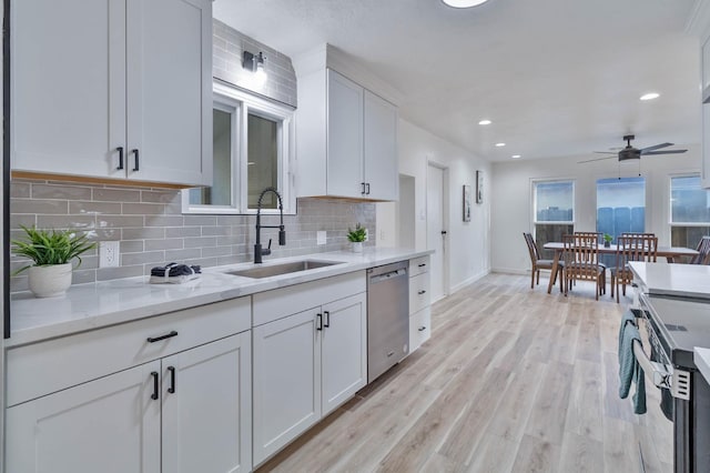 kitchen with stainless steel appliances, decorative backsplash, light wood-style floors, white cabinetry, and a sink