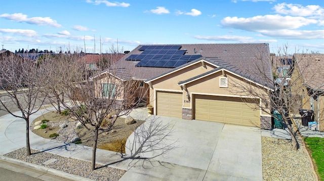 view of front of home with an attached garage, solar panels, stone siding, driveway, and stucco siding