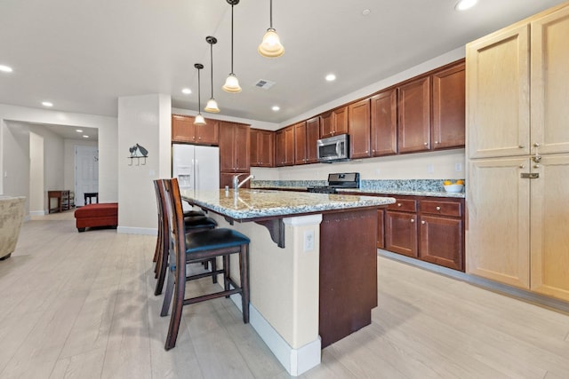 kitchen featuring light stone counters, stainless steel appliances, visible vents, a sink, and light wood-type flooring