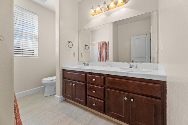 bathroom featuring double vanity, a sink, baseboards, and wood finished floors