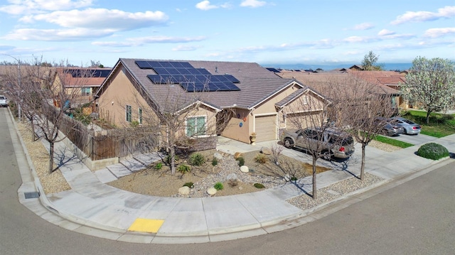 view of front of home featuring concrete driveway, solar panels, an attached garage, fence, and stucco siding