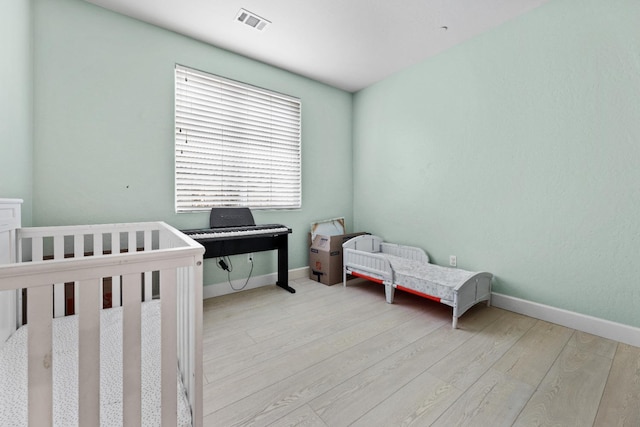 bedroom with a nursery area, visible vents, baseboards, and wood finished floors