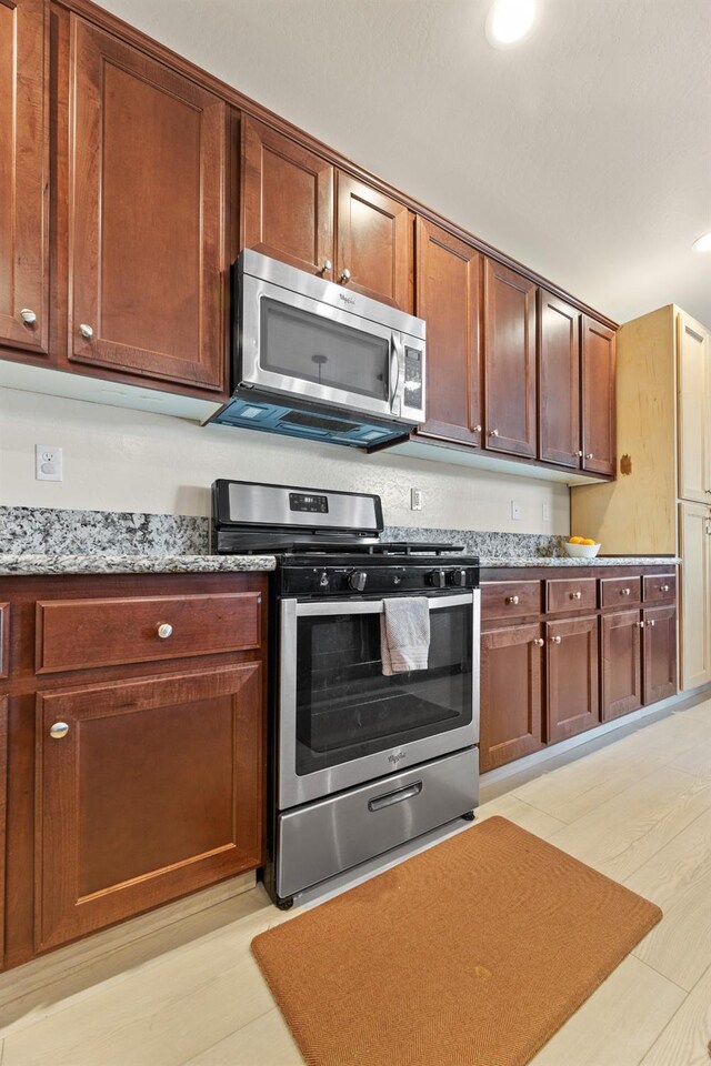 kitchen featuring stainless steel appliances, recessed lighting, light wood-style floors, and light stone counters