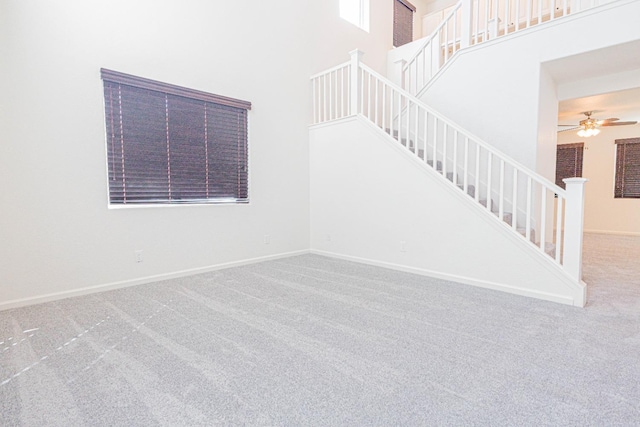 interior space featuring carpet flooring, baseboards, a towering ceiling, and ceiling fan