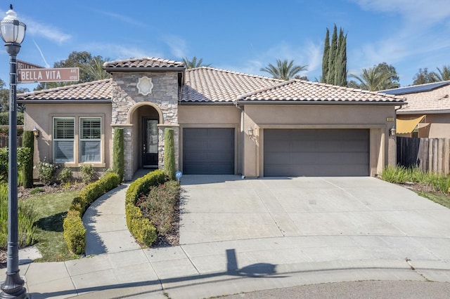 mediterranean / spanish house with concrete driveway, stone siding, a tiled roof, an attached garage, and stucco siding